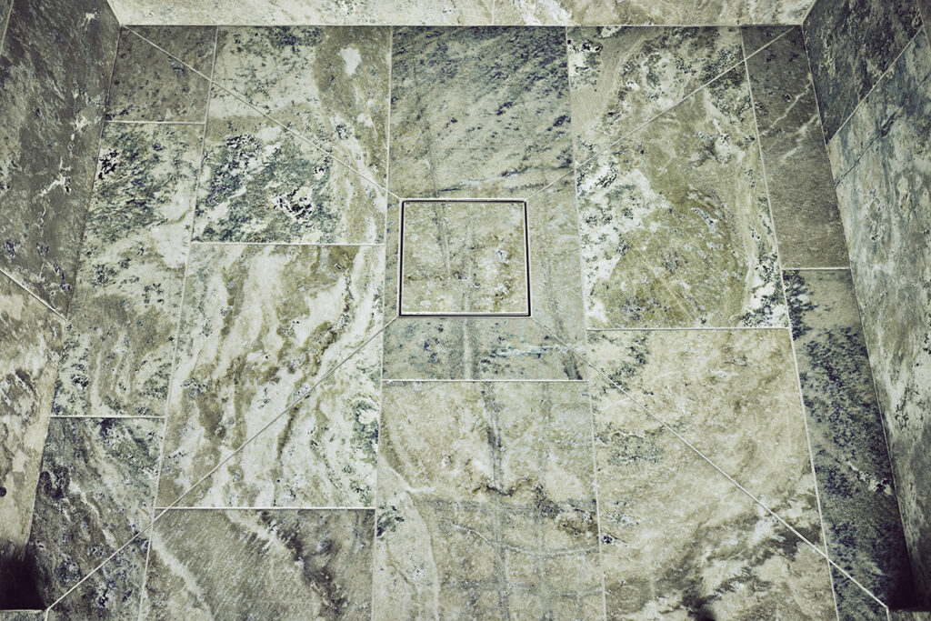 A Purus Square Tile Insert grate shown installed in a Swedish Green Marble wetroom floor.
