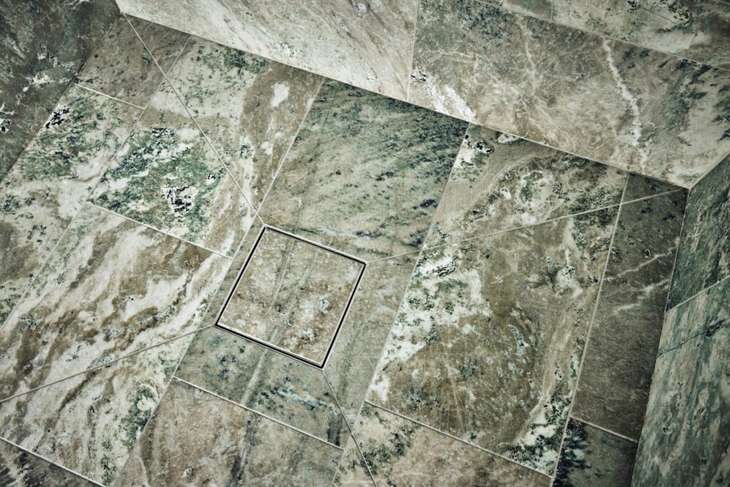 A Purus Square Tile Insert grate shown installed in a Swedish Green Marble wetroom floor.
